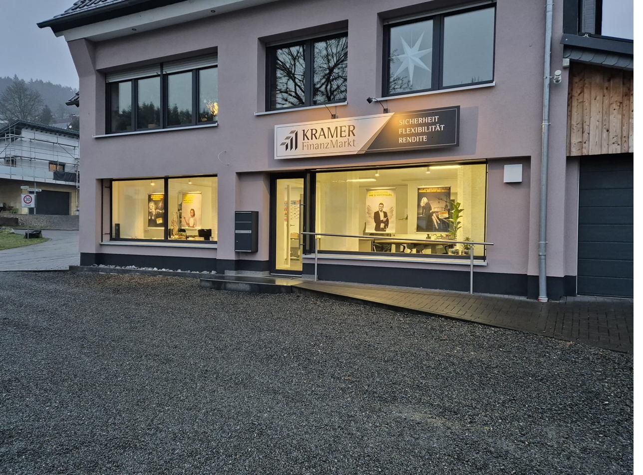 Das beleuchtete Ladenlokal von KRAMER FinanzMarkt am Abend